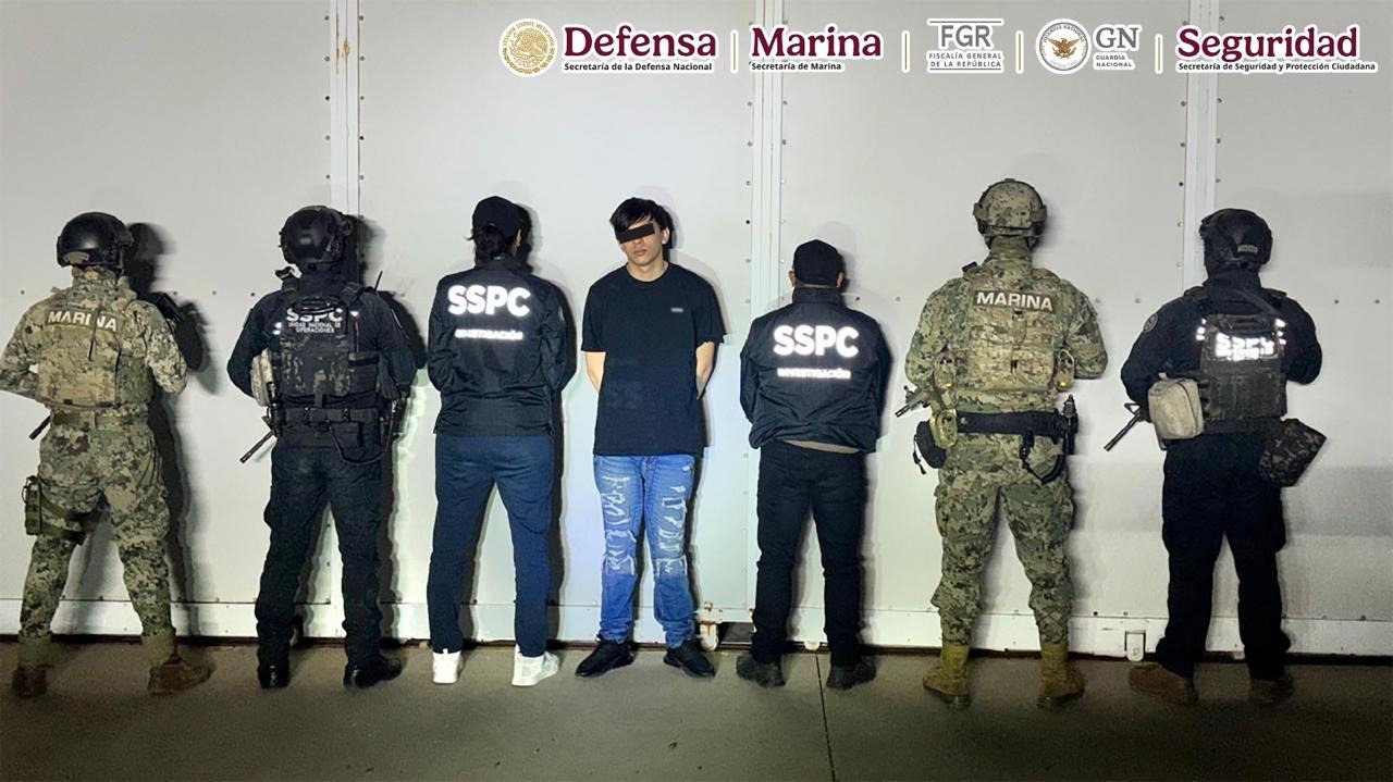 Persona detenida con una linea negra en los ojos junto a elementos de seguridad