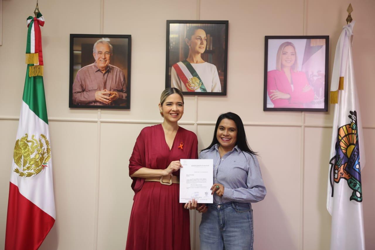 Estrella Palacios junto a Isis Vidal y bandera de México con cuadros de Rubén Rocha Moya y Claudia Sheinbaum