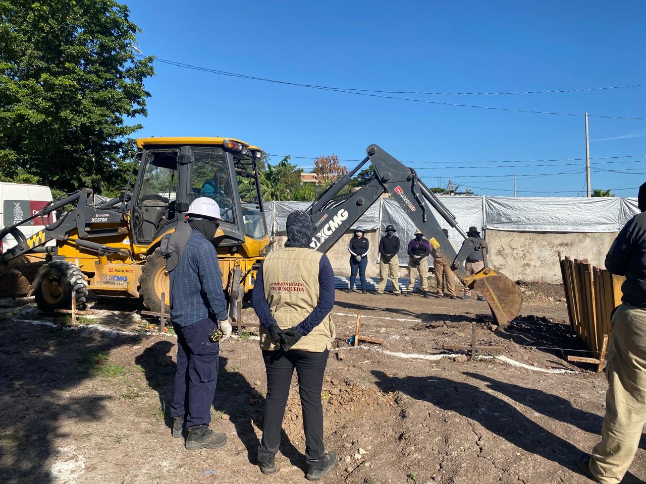 Maquinaria pesada realizando labores de excavación, con personal en campo que porta chalecos y cascos de seguridad, uno de ellos lleva la identificación de la Comisión Estatal de Búsqueda, mientras observan el trabajo desde una corta distancia dentro del panteón 21 de Marzo, en Culiacán