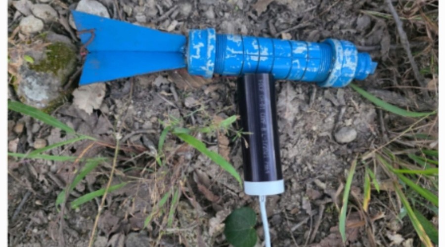 Artefacto metálico de color azul tirado sobre tierra y pasto, parece ser un proyectil o un artefacto explosivo colocado en el suelo