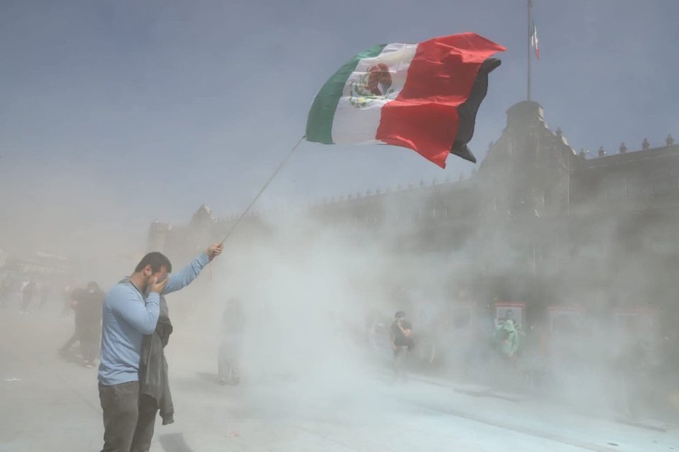 Un hombre sostiene una bandera de México en medio del humo de extintores en la marcha de la Generación Z