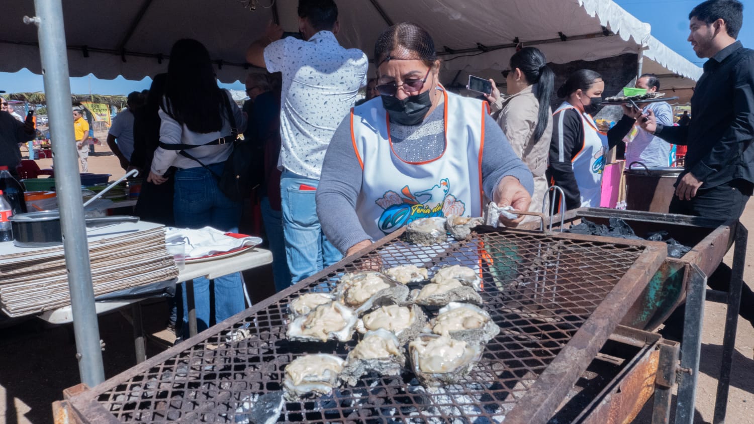Mujer poniendo sobre un asador ostiones para preparar