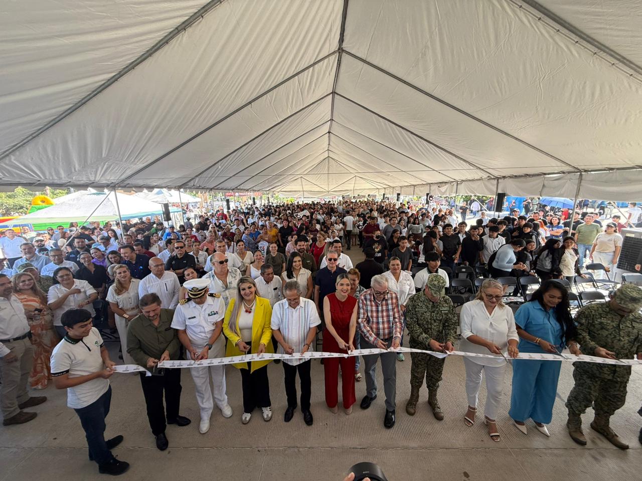 El gobernador de Sinaloa y la alcaldesa de Mazatlán junto a autoridades de seguridad y gubernamentales sosteniendo un listón y por detrás de ellos un gran grupo de personas debajo de una carpa
