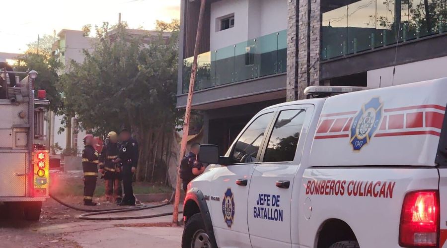 Elementos del cuerpo de bomberos junto a una unidad de bomberos y un camión frente a una casa vandalizada