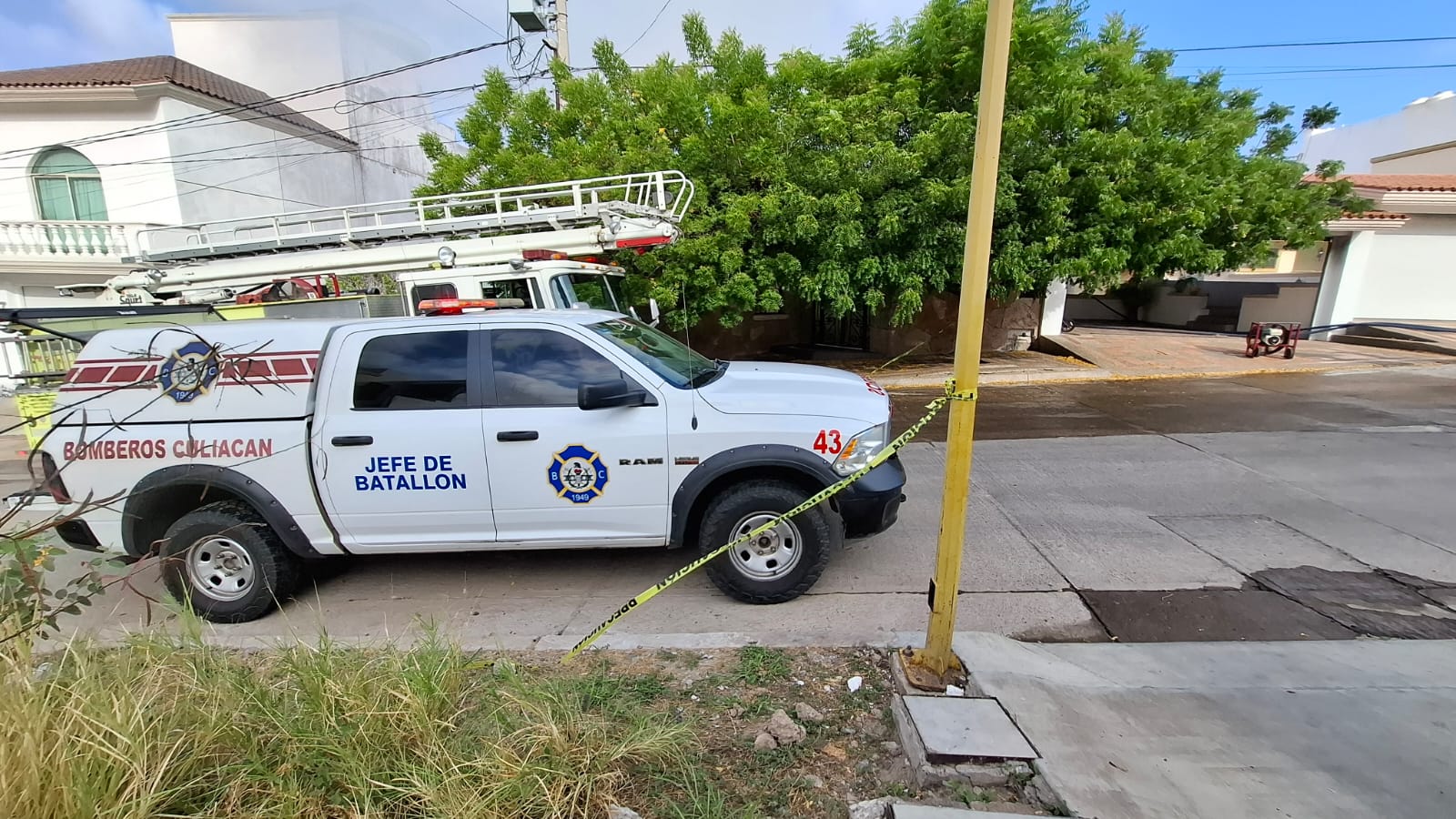 Camioneta blanca de Bomberos Culiacán y detrás una casa incendiada en Culiacán