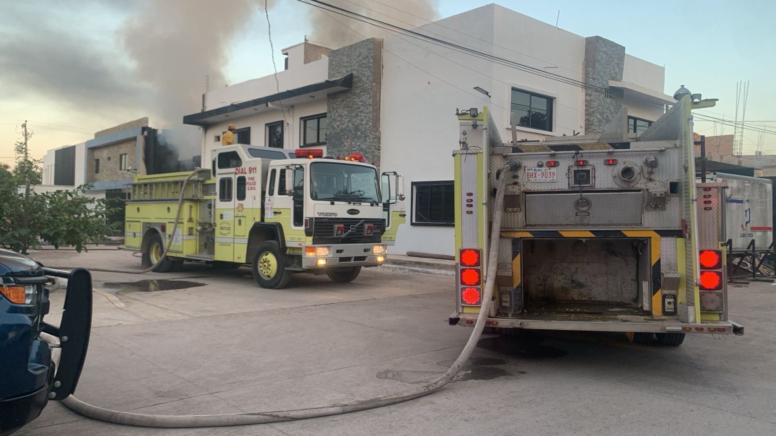 Dos ca,miones de bomberos junto a un edificio con fuego y humo negro