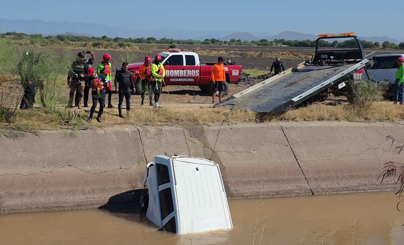 Grupo de Bomberos jalando con una cuerda y una grúa la camioneta que está al interior de un canal