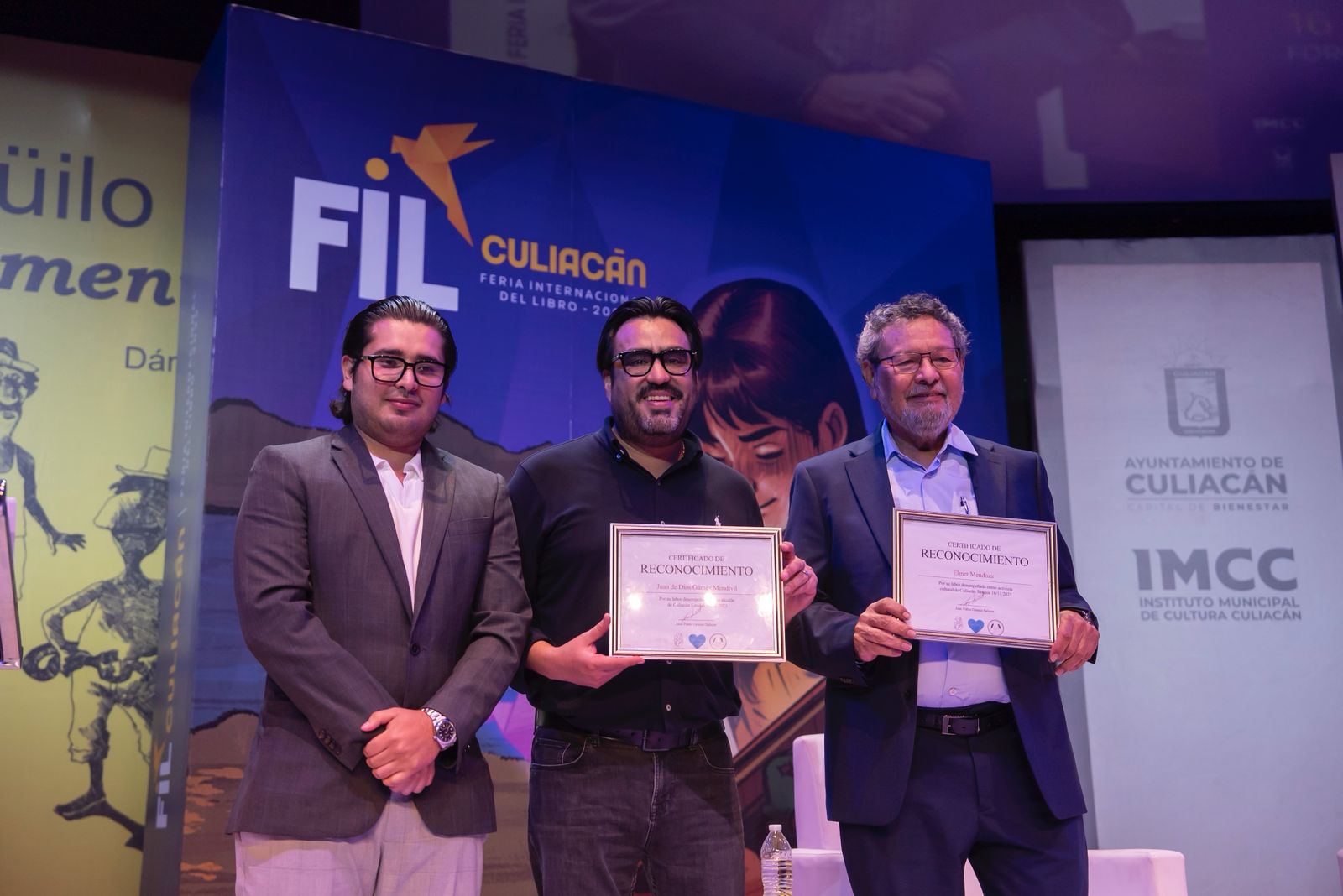 Juan de Dios Gámez junto a unos asistentes sosteniendo unos reconocimientos en la FIL Culiacán