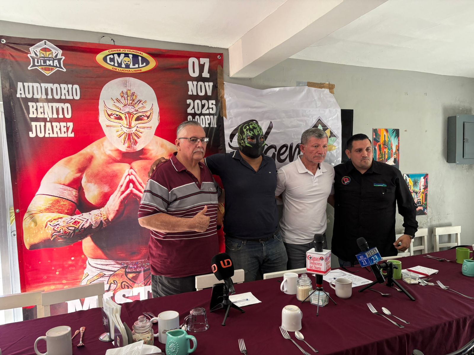 Autoridades de IMDA, organizadores de ULMA y luchador posando para foto durante una conferencia de prensa donde se puede ver detrás de los mismos un cartel promocional del show.