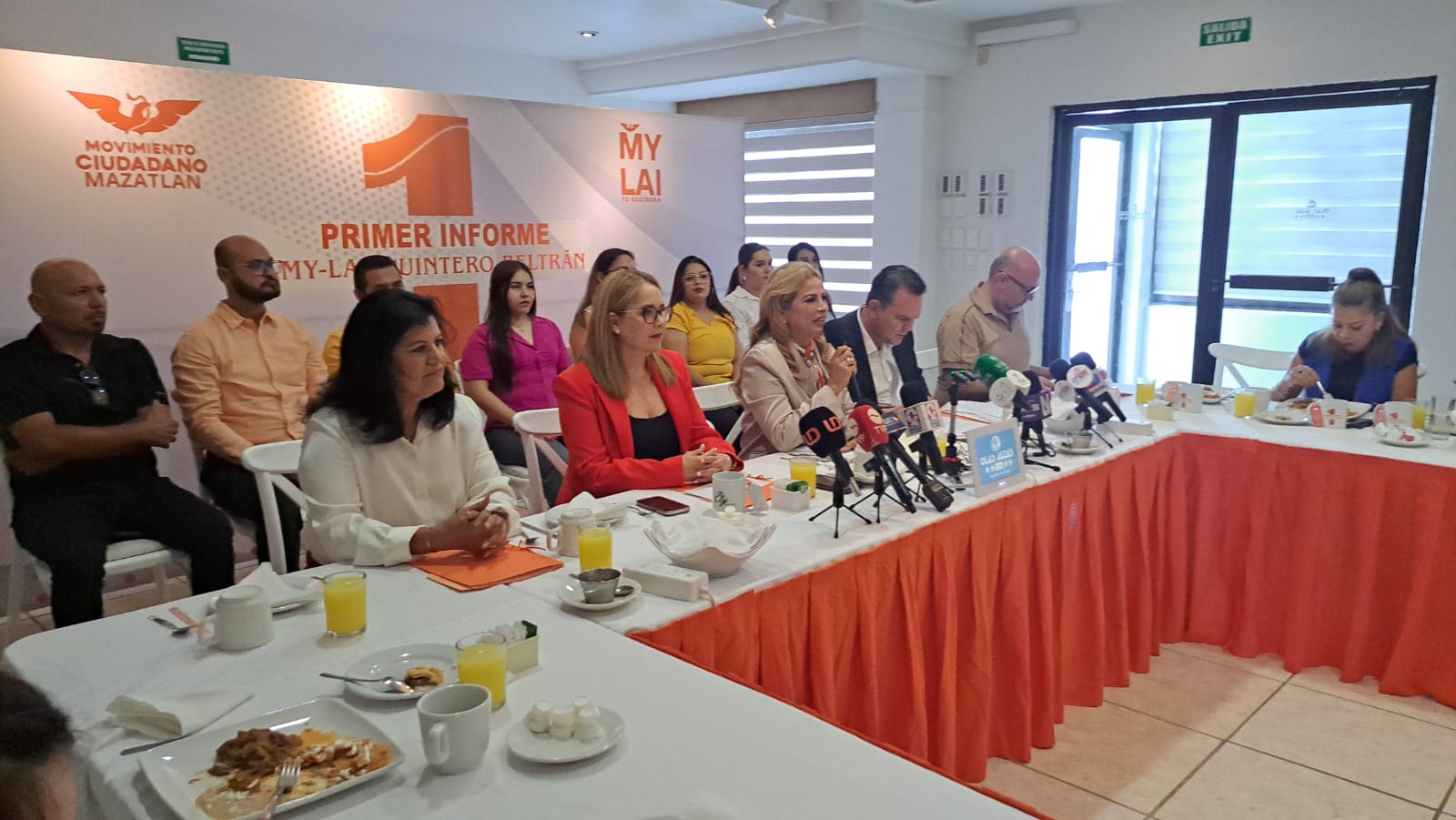 My-Lai Quintero presenta su primer informe como regidora del partido Movimiento ciudadano, se ve a la regidora en el medio de la mesa dando declaraciones a los medios de comunicación y alrededor mas un grupo de personas que acompañan la sesión.