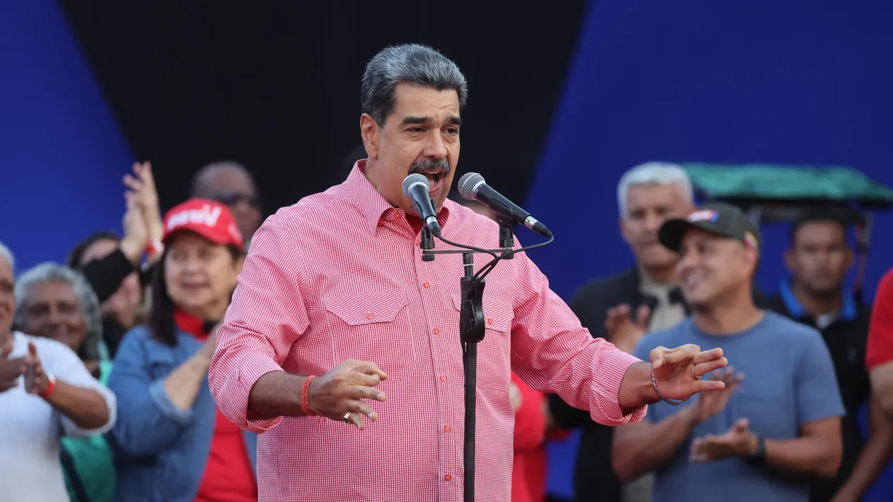 El presidente de Venezuela Nicolas Maduro dando un discurso publico con un micrófono en un tripee y el con los brazos estirados hacia el frente