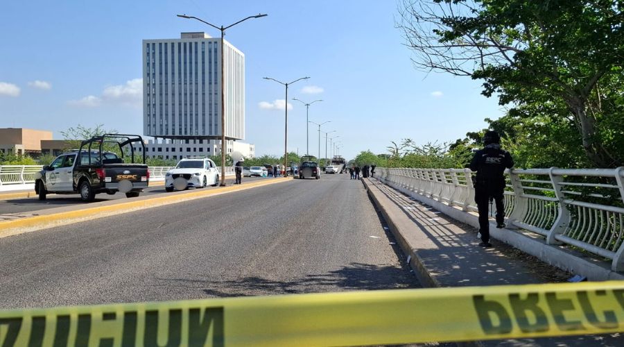 Cinta amarilla de precaución y un elemento policiaco, al fondo se osbervan varias unidades de diferentes corporaciones policiacas y 3 vehículos, uno de ellos subiendo a una grúa