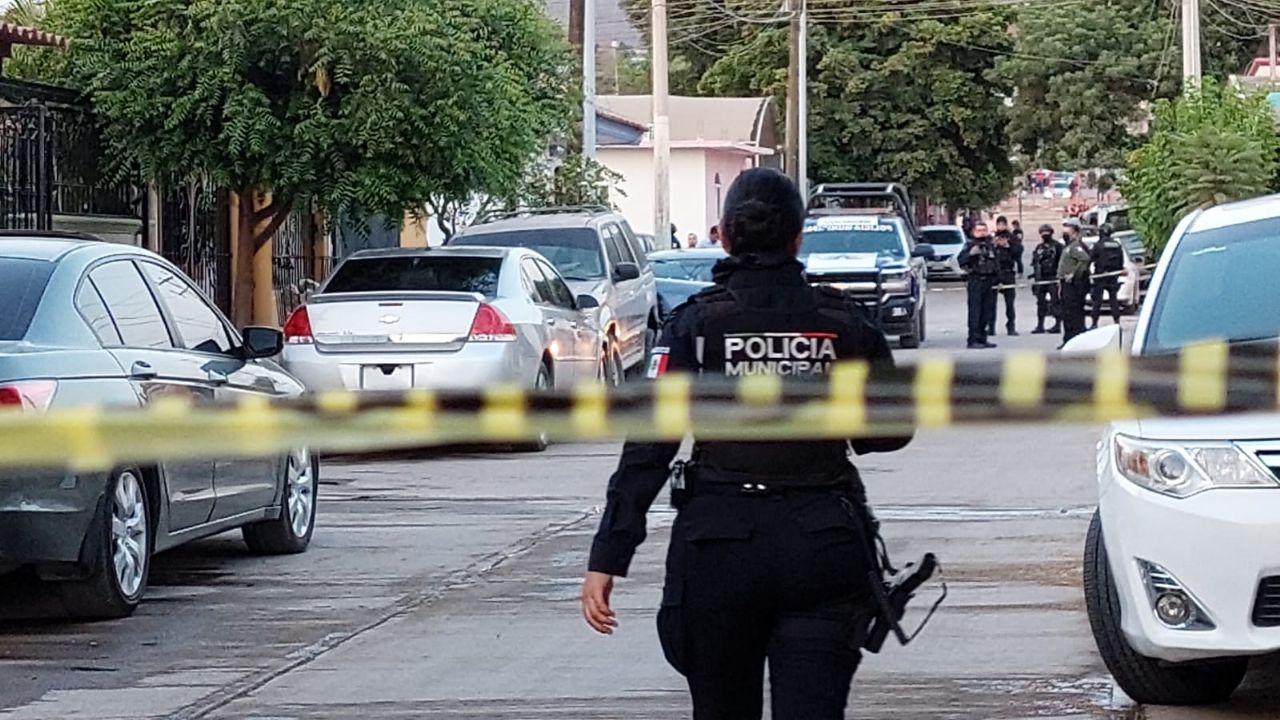 Policía caminando dentro de una zona acordonada y al fondo hay más policías