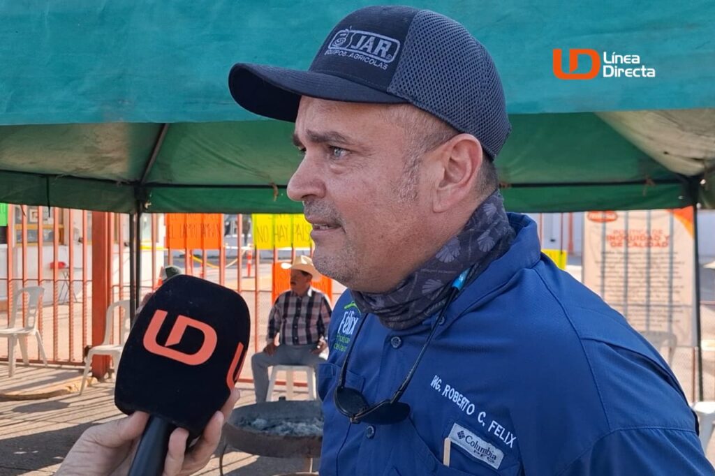 Hombre con cachucha y camisa azul hablando hacia un micrófono negro con calcomanía color naranja de las letras LD