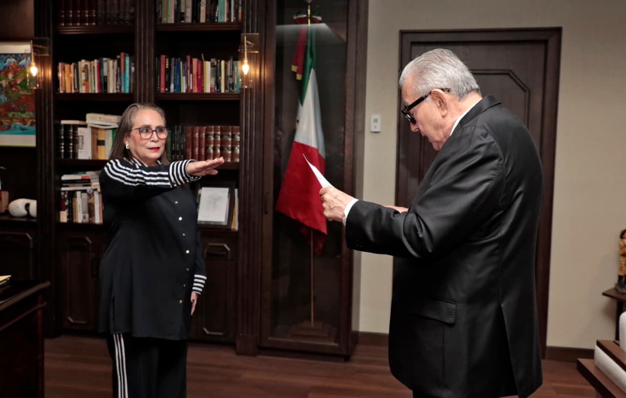 El gobernador de Sinaloa Rubén Rocha Moya leyendo un documento frente a Silvia Evelin Ward Bringas quien esta con el brazo levantado hacia delante en toma de protesta para ser nombrada como subsecretaria de Educación Básica en Sinaloa