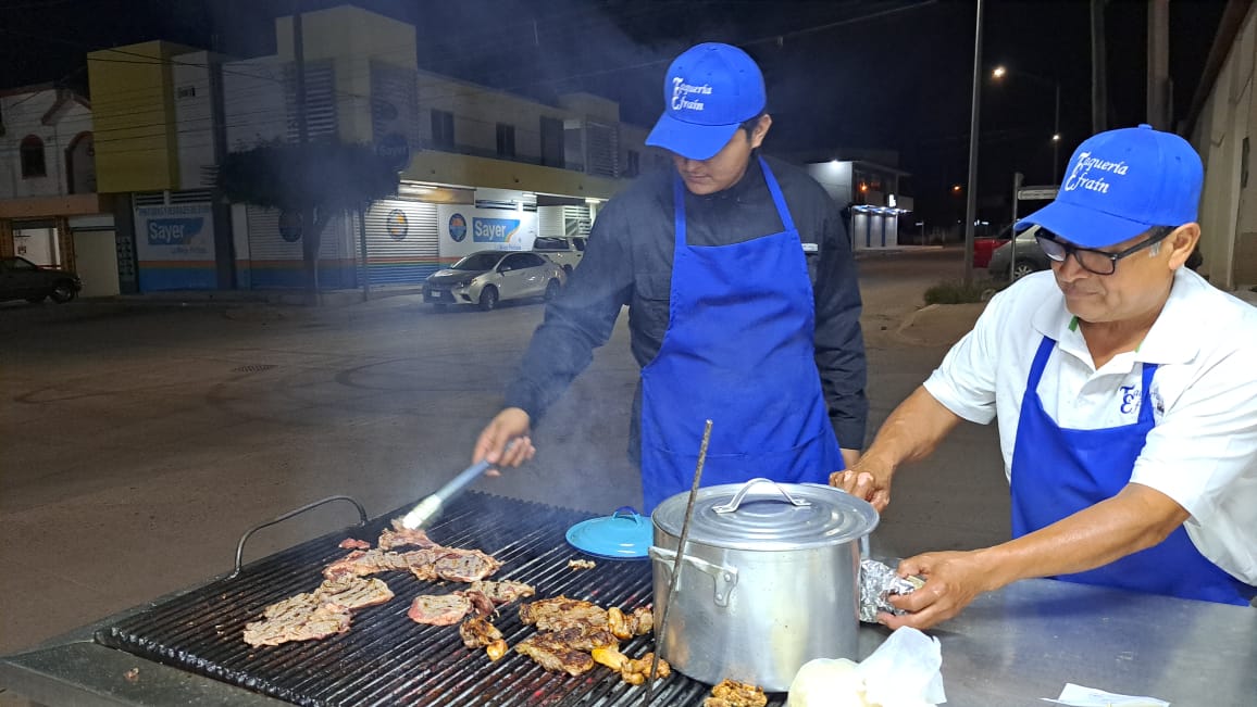 Dos personas con gorra azul asando carne