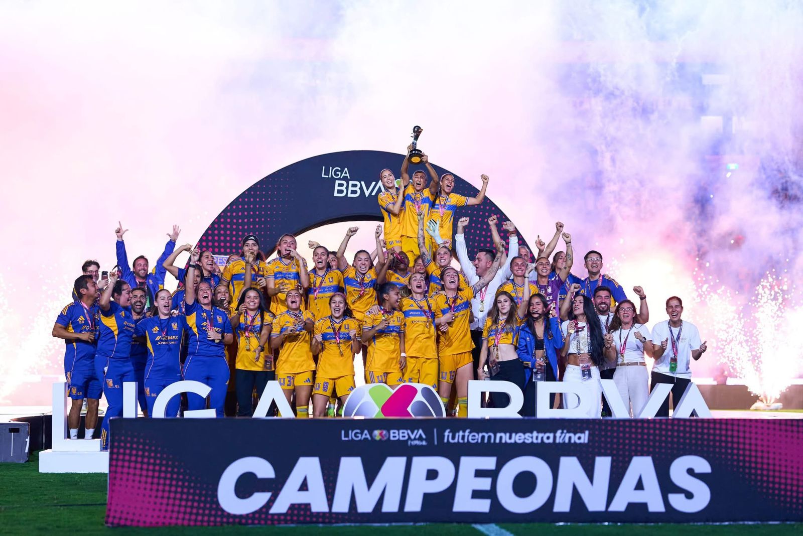 El plantel de Tigres Femenil levantando el titulo de Liga Mx y por detrás sale humo de color rosa