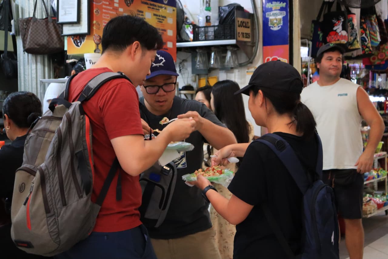 Tres personas comiendo un platillo al interior de un mercado