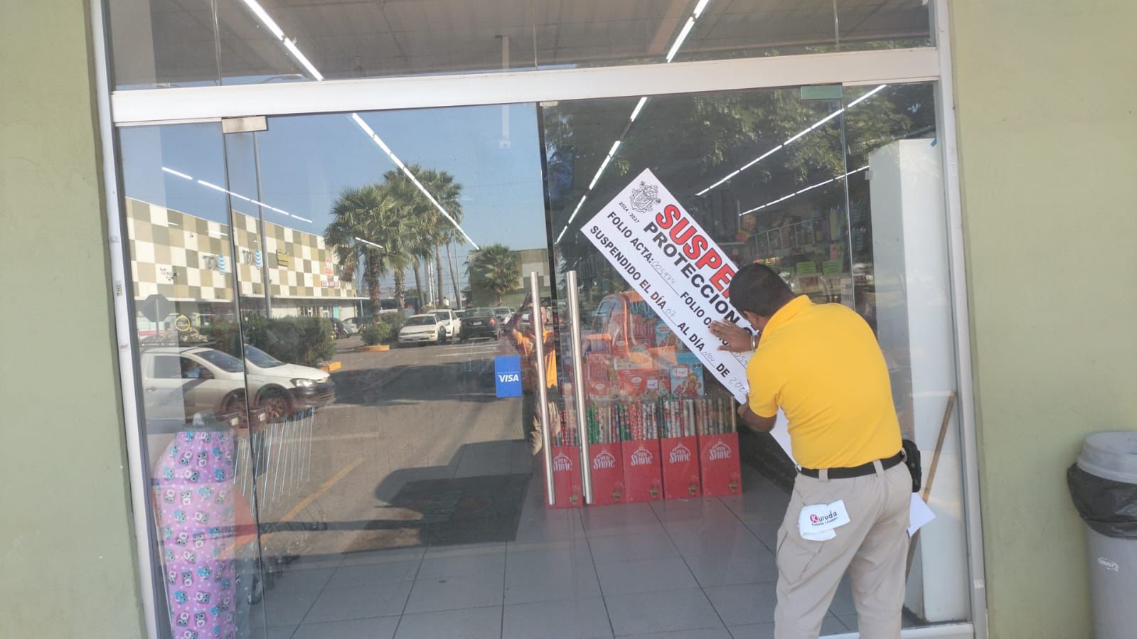 Elemento de Protección Civil colocando logo de clausurado a la puerta principal de una tienda Waldo s en Mazatlán