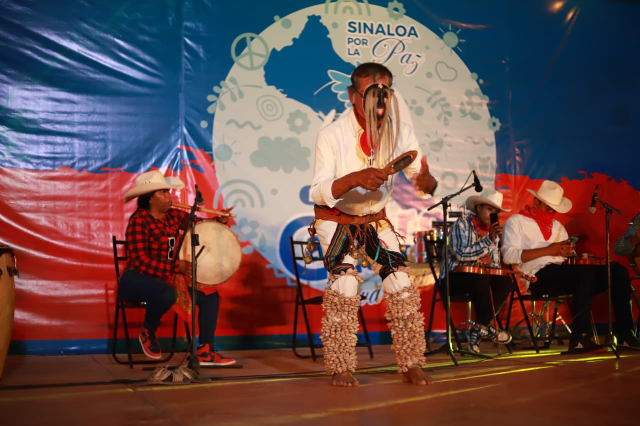 Hombre baila la danza del venado en un escenario con fondo azul y rojo