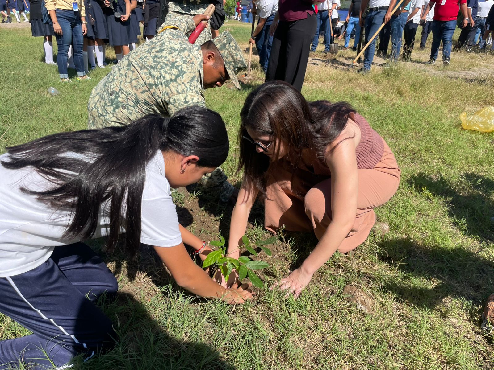 Niña y dos adultos hincados plantando un árbol