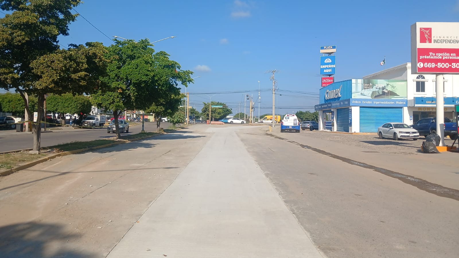 Calle semi pavimentada, de lado izquierdo se ven árboles, del lado derecho negocios
