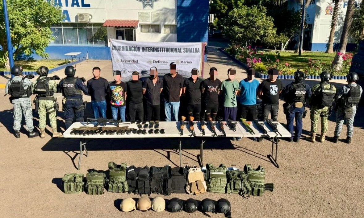 Elementos de la marina junto a personas detenidas, en una mesa hay armas y en el suelo sobre una lona hay equipo asegurado
