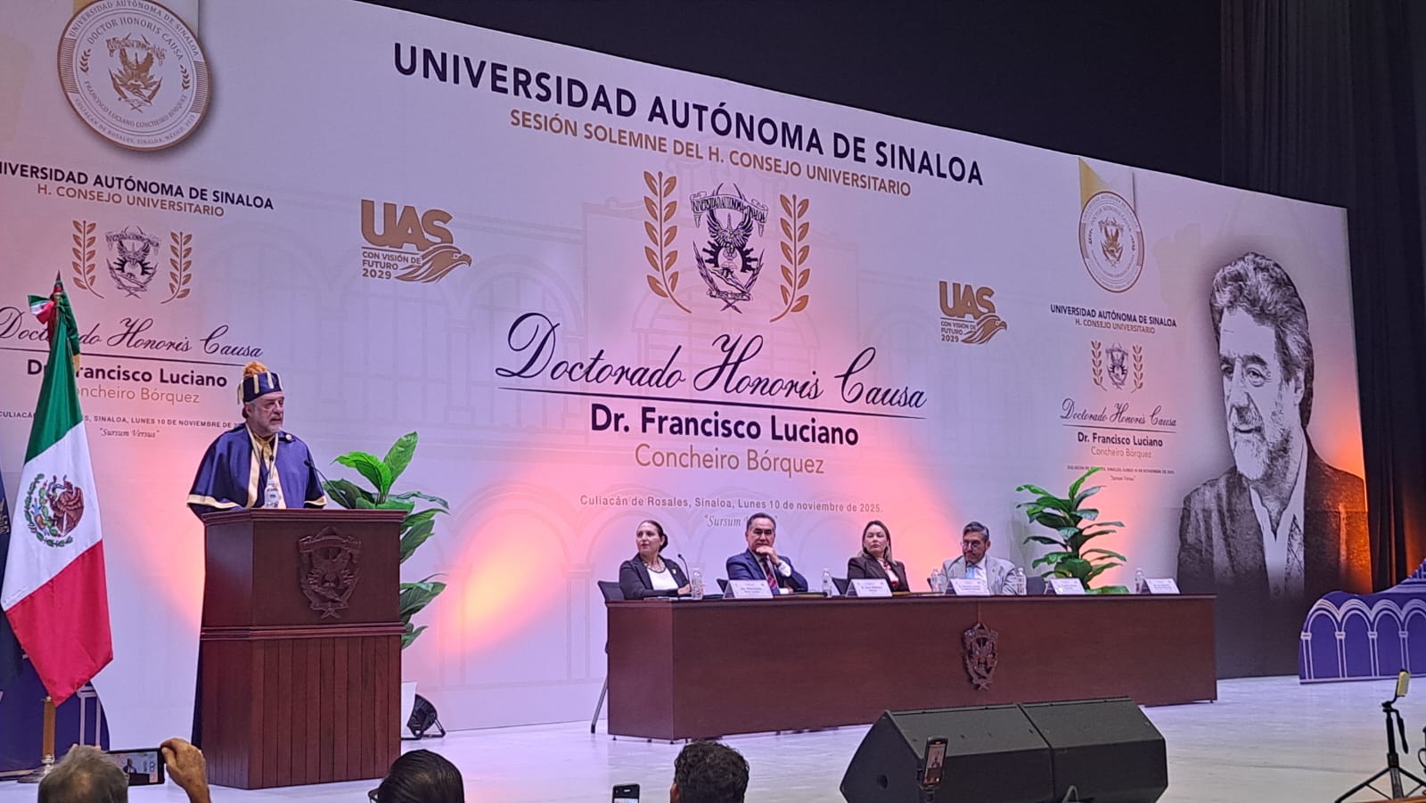 Luciano Concheiro en podium, a lado derecho hay una mesa con autoridades de la UAS