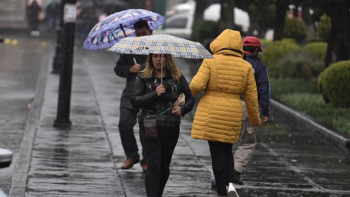 PErsonas aabrigadas con chamarras y con paraguas por la lluvia y el frío