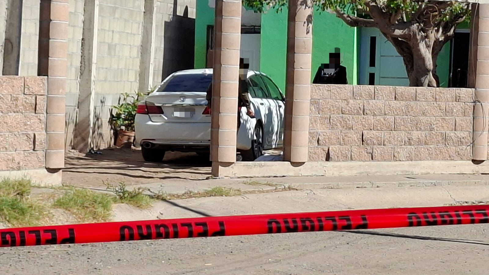 Cinta roja de precaución frente a una casa color verde y un carro blanco