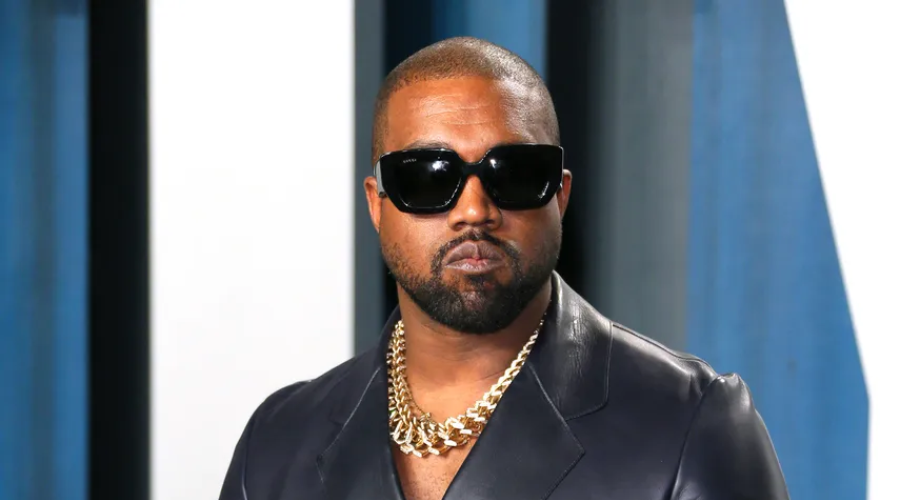 El cantante Kany West con lentes negros y traje negro con collar dorado