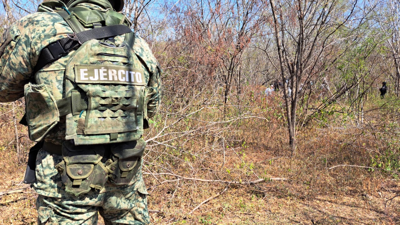 Elemento del ejercito de espaldas en un monte, al fondo personas en que encontraron una osamenta al sur de Culiacán