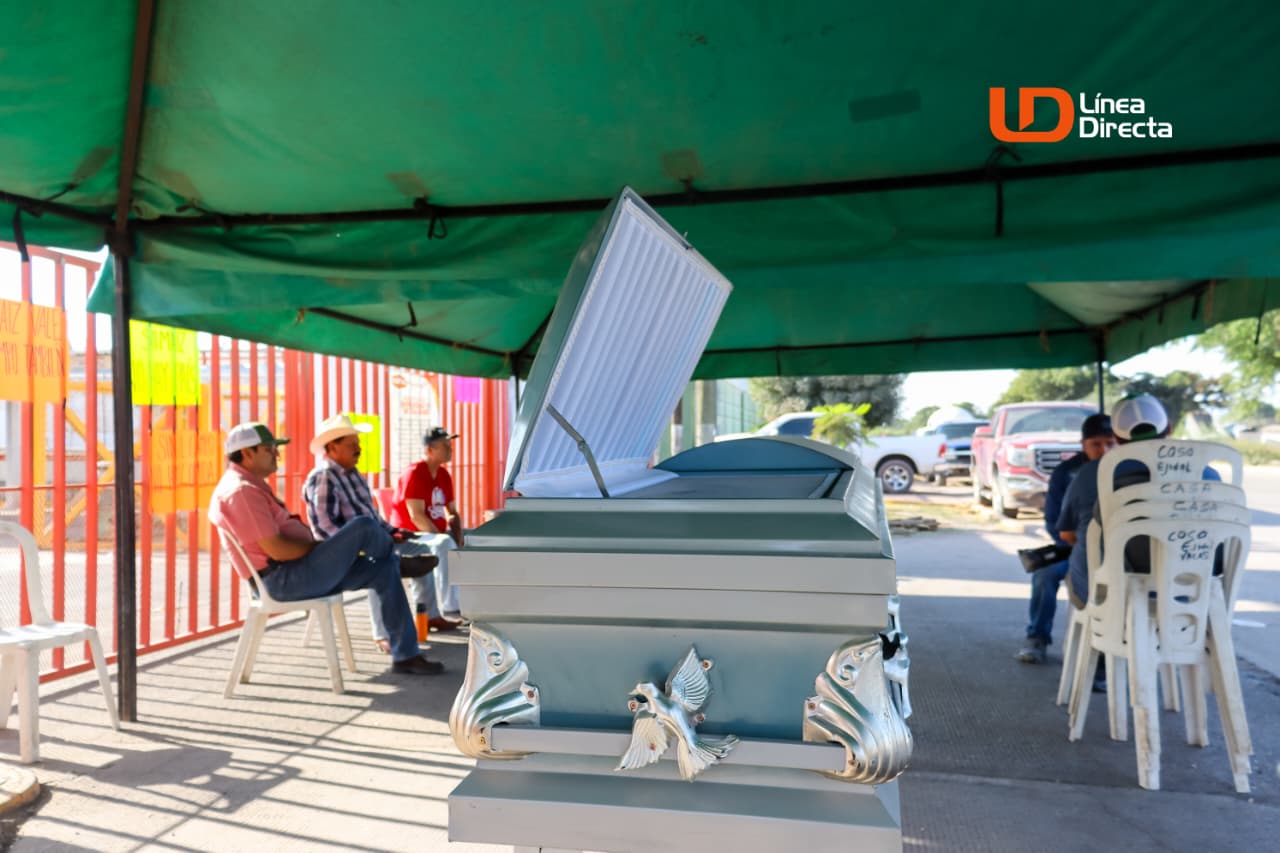 Féretro abierto color gris y personas sentadas en sillas