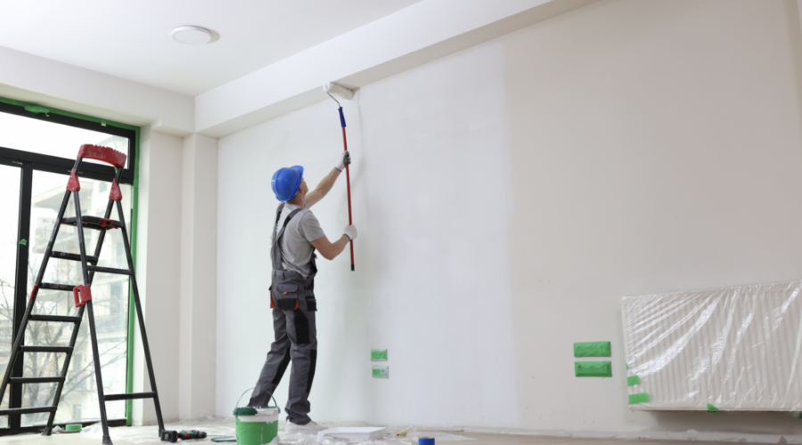 Persona pintando la pared de una casa junto a él una escalera y una cubeta