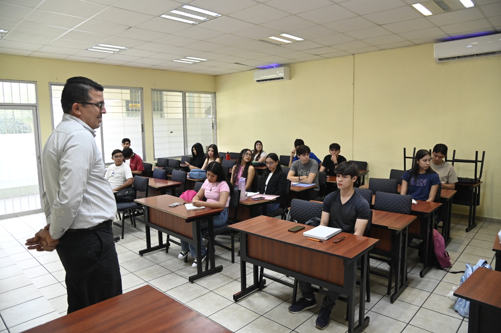 Profesor dando clases en una escuela con alumnos sentados en mesa bancos