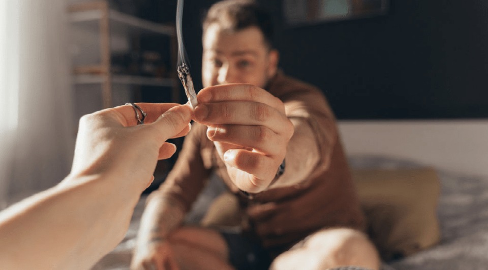 joven estira la mano y agarra un cigarro de mariguana