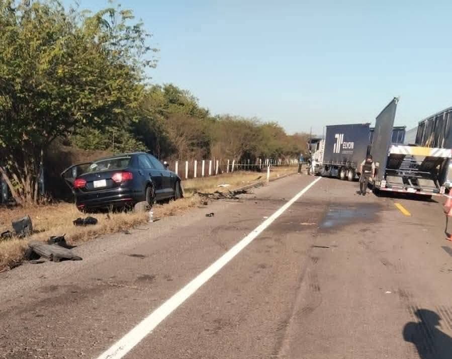 Vehículo negro con daños y al lado un tráiler tipo nodriza.