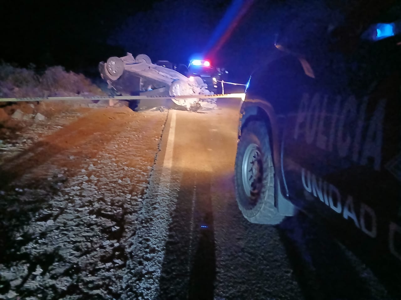 Vehículo volcado en una carretera, se observa una cinta amarilla de precaución así como una unidad policiaca