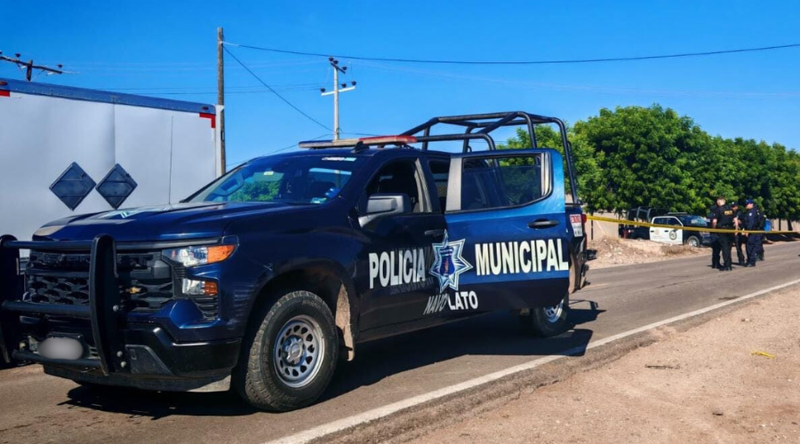 Unidad de la policía municipal de Navolato estacionada y con la puerta trasera abierta, por detrás elementos y el área asegurada con cinta amarilla
