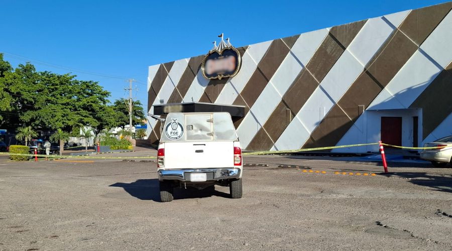 Fachada de un establecimiento con lineas diagonales en blanco y café y en el estacionamiento una unidad de la FGE y otra de policía, se observa un carro color café claro