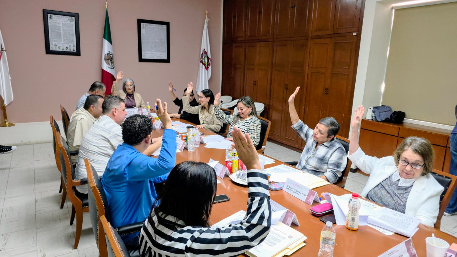 Personas sentadas en una mesa redonda y levantando la mano