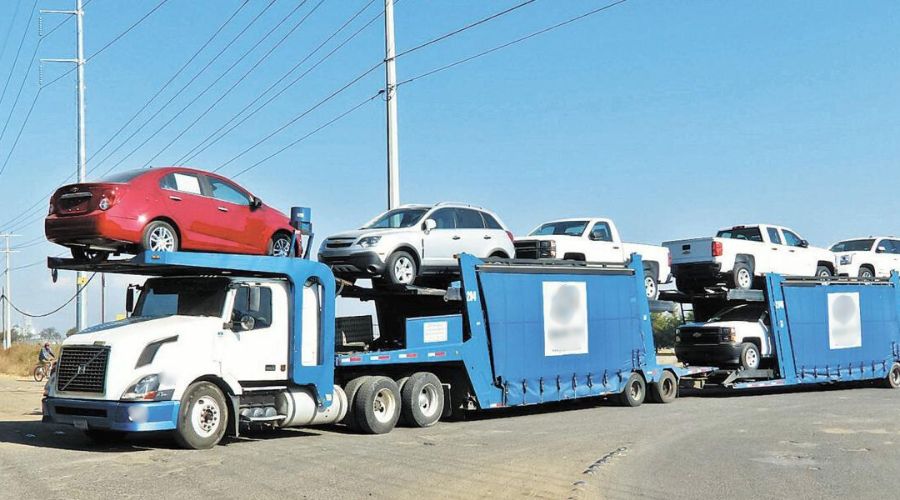 Tráiler de carga con carros de diferentes colores en una carretera