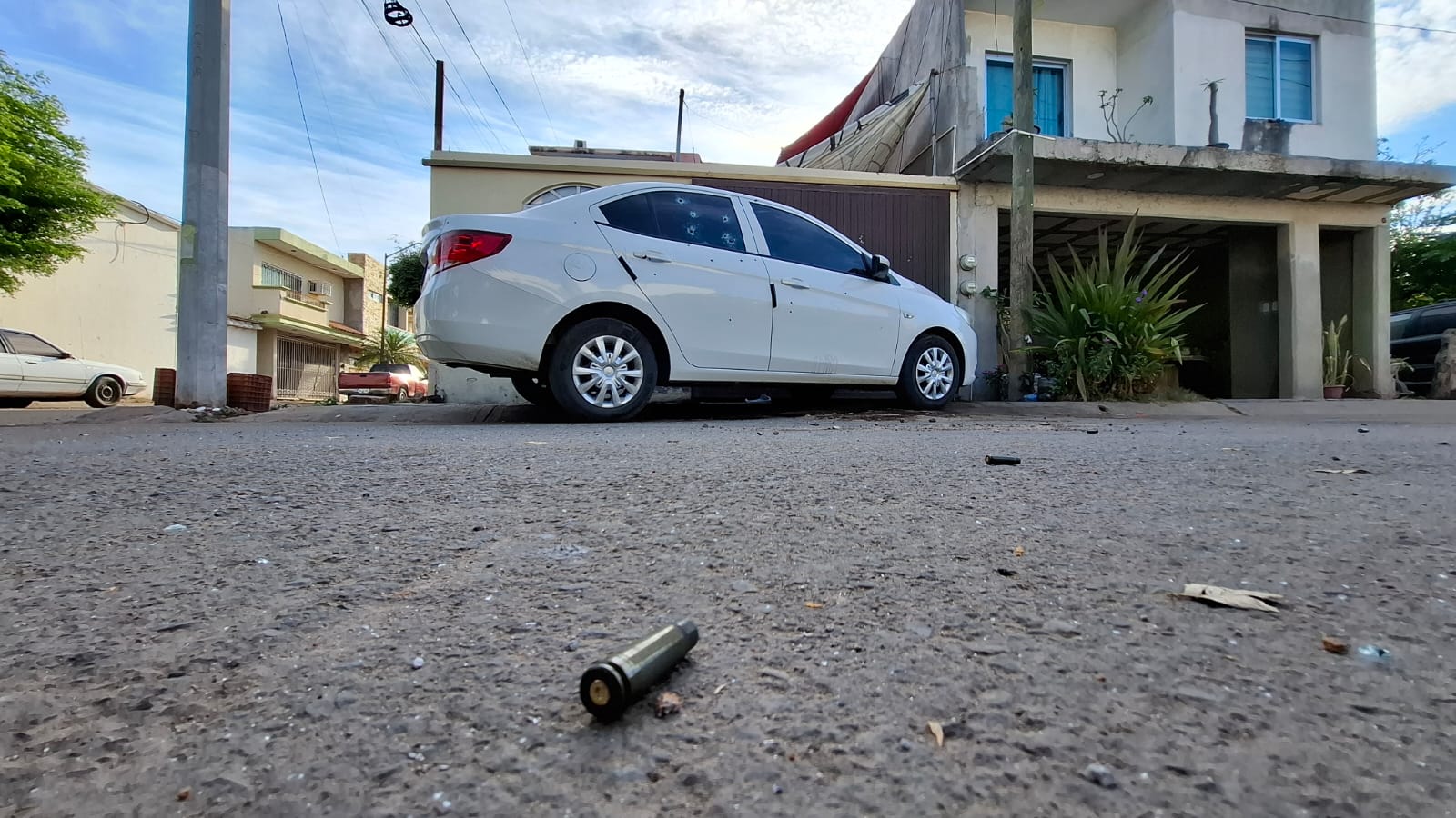 casquillo de arma en el suelo, al fondo se observa un carro color blanco y un domicilio con impactos de bala