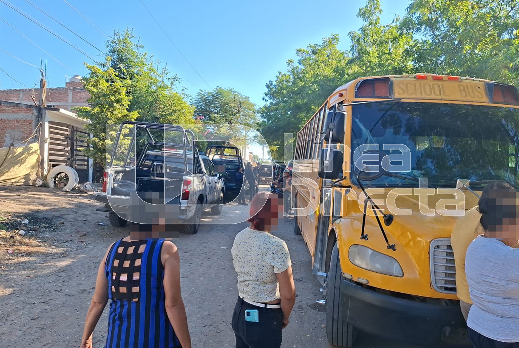 Personas viendo hacia el fondo, un camión amarillo y carros y casas en un vecindario
