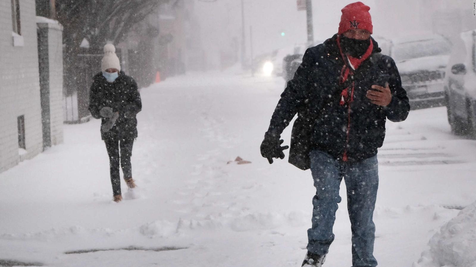 Dos personas caminan en la nieve con gorro, bufandas y guante