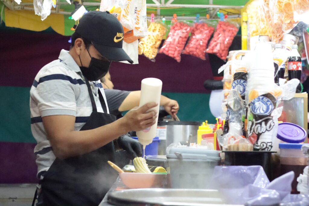 Puesto de venta de elotes preparados donde se ve a un comerciante preparando el prducto