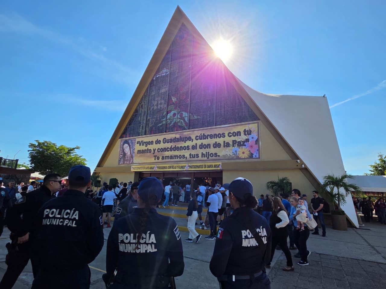 Elementos de la policía municipal afuera de una Iglesia con más personas, y sol fuerte en el cielo