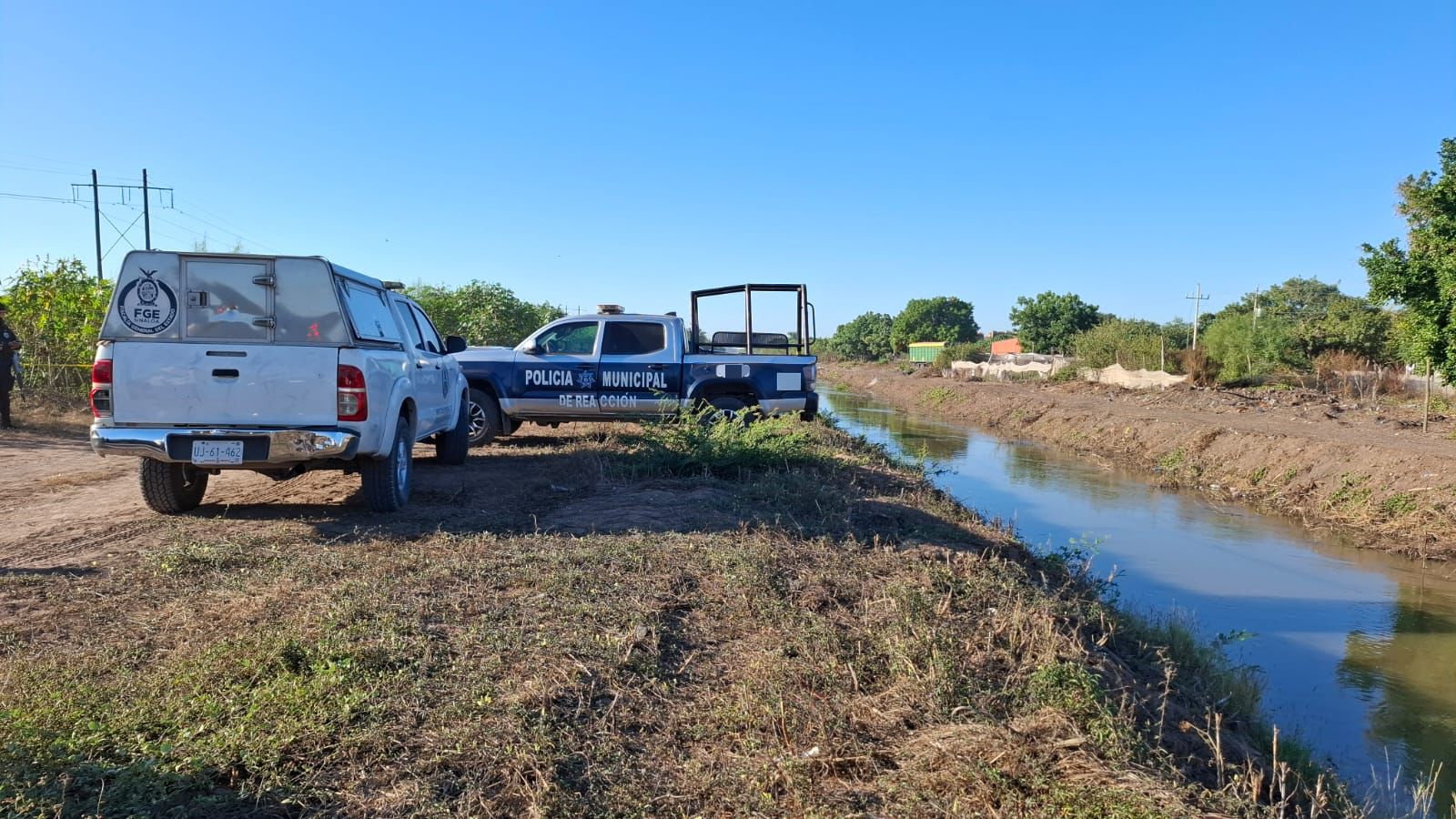 Patrulla de la Policía Municipal de Navolato y una unidad de la FGE al lado de un canal de riego