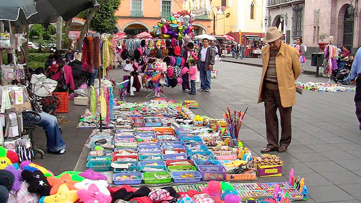 Personas caminando frente a puestos en la banqueta