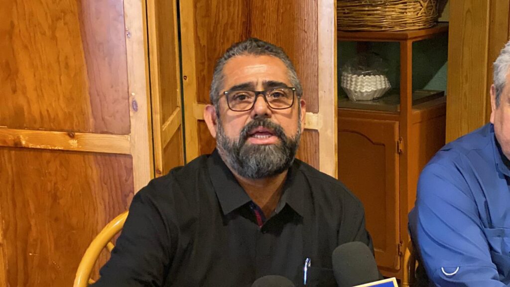 Persona con camisa negra y lentes de frente hablando